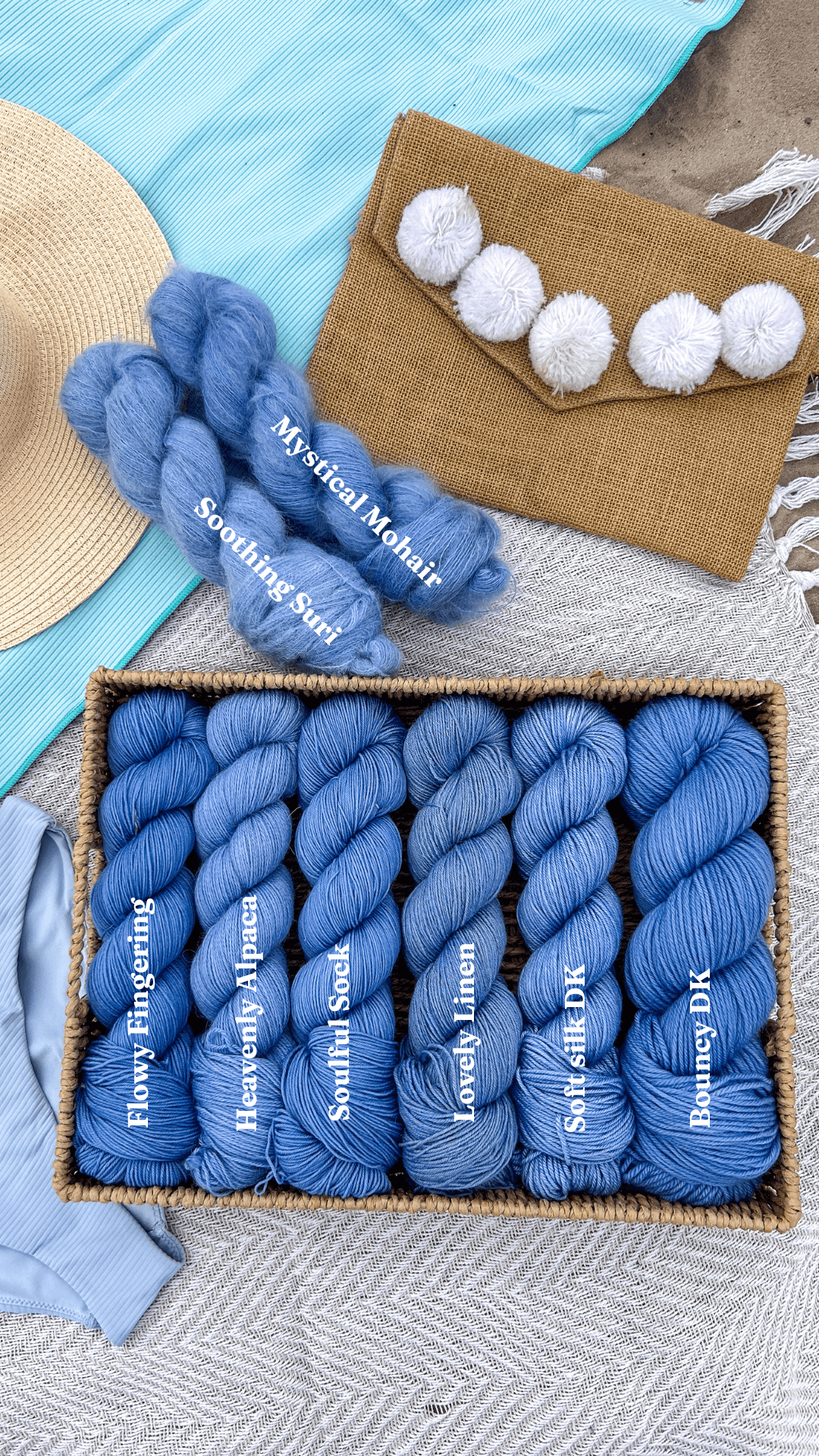 Box of blue yarn with labels, a burlap bag with pom-poms, and a straw hat on a textured surface.