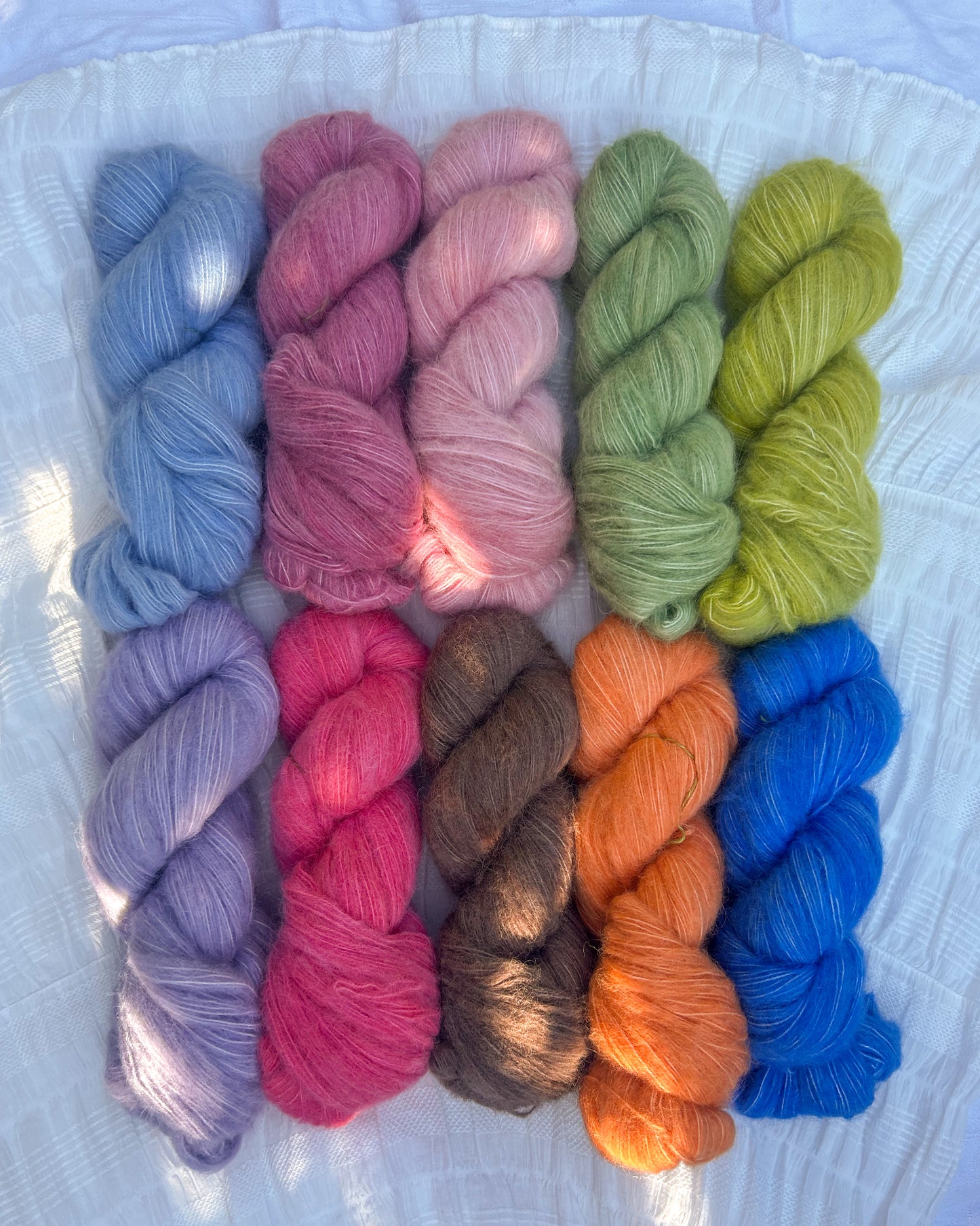 Assorted colorful yarn skeins on an alpaca base on a textured white surface