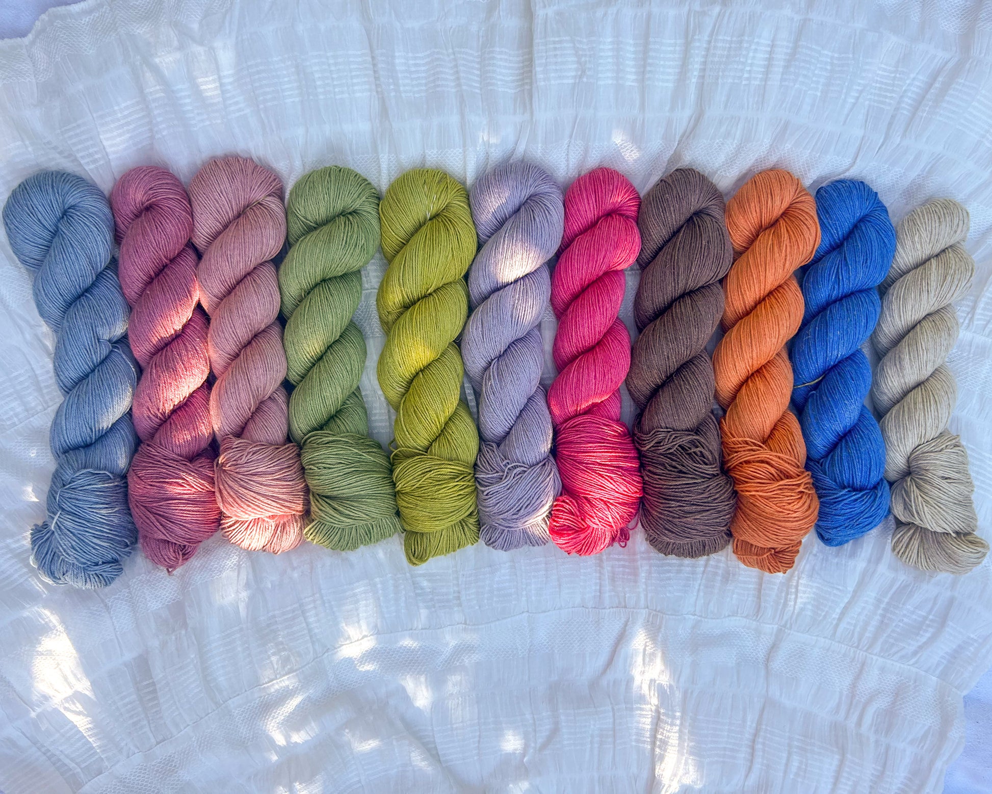 Row of colorful yarn skeins on linen merino base on a textured white background
