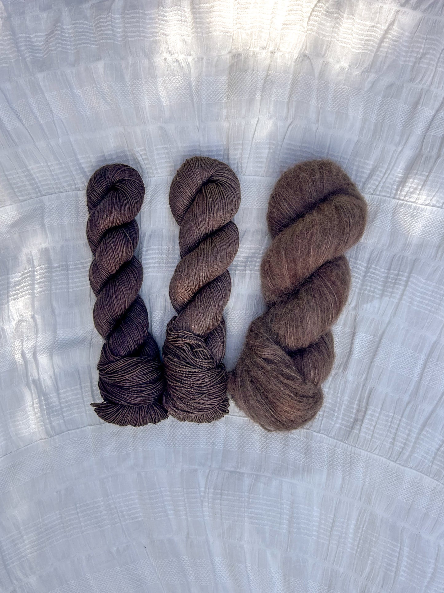 Three skeins of brown yarn on a textured white surface