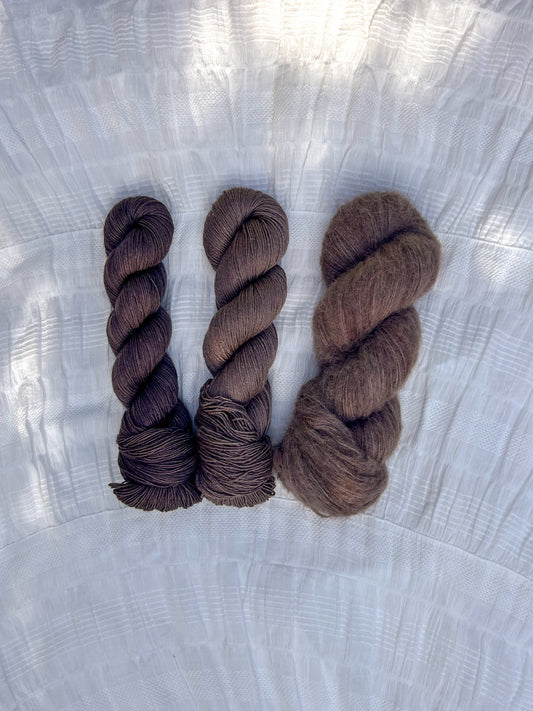 Three skeins of brown yarn on a textured white surface
